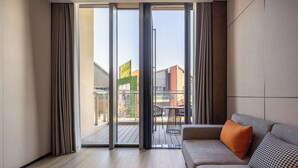 A modern living room with a sofa, a patterned cushion, and a sliding glass door leading to an outdoor deck. - UrCove by Hyatt Taicang South Railway (Suzhou)
