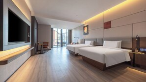 A modern hotel room with a large flat-screen TV, a sofa, two beds, a desk, and a view of the city. - UrCove by Hyatt Taicang South Railway (Suzhou)