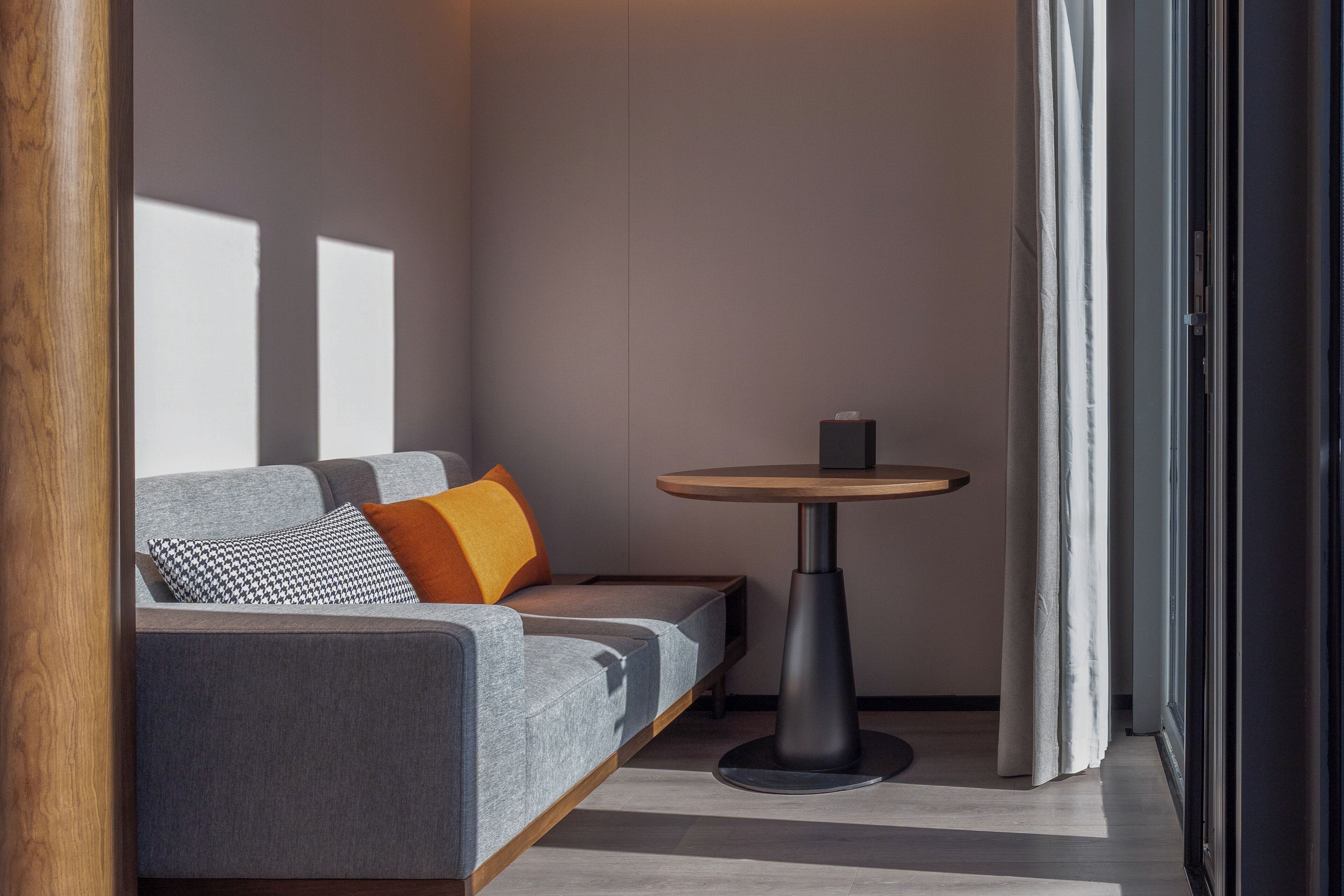 Ein modernes Zimmer mit grauem Sofa, rundem Tisch und Holzboden.