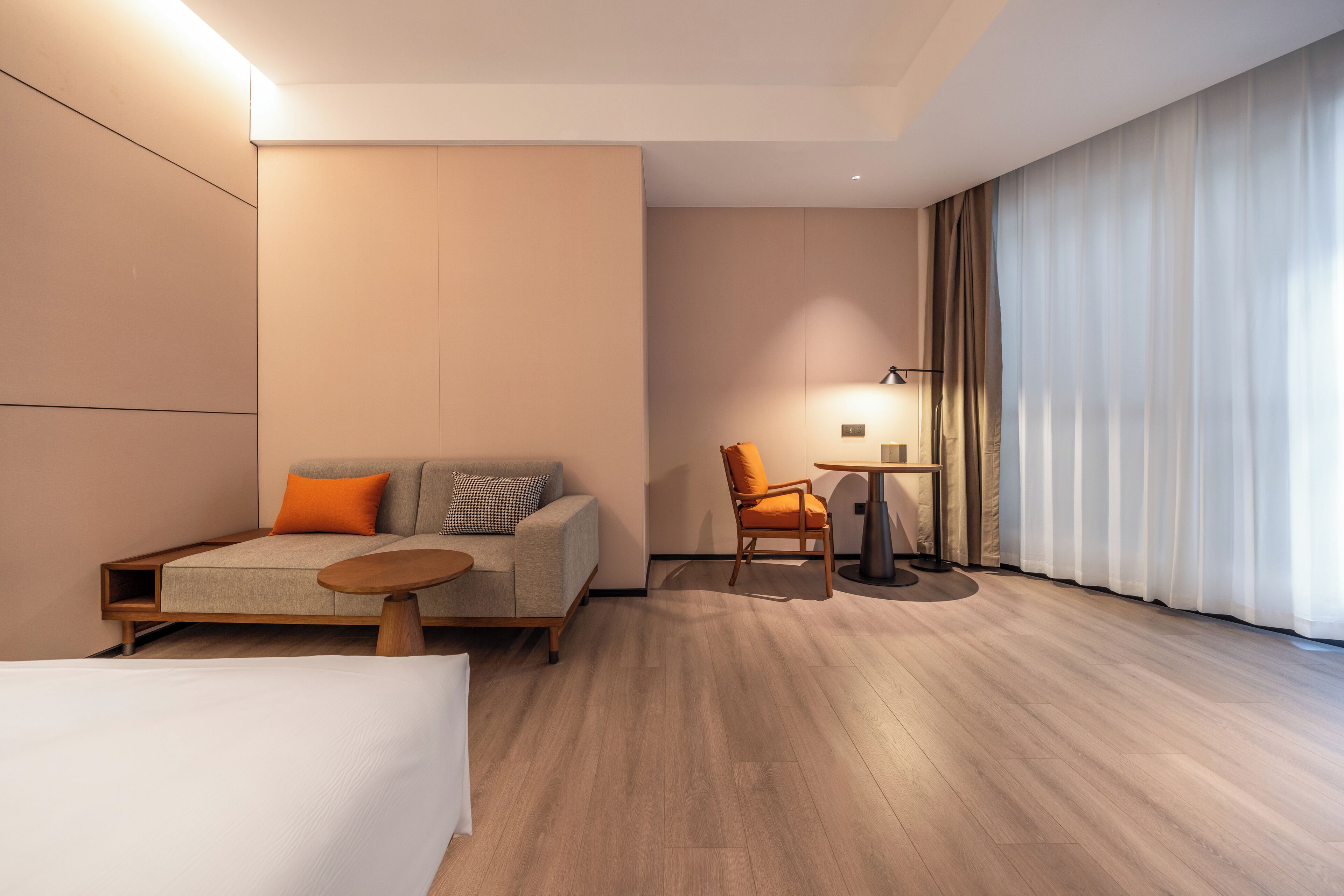 Een moderne hotelkamer met een bank, fauteuil, klein tafeltje en een groot raam met gordijnen.
