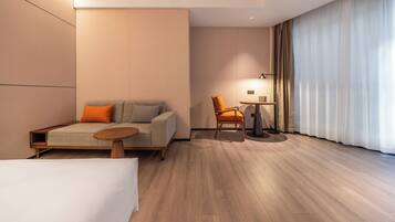 Een moderne hotelkamer met een bank, fauteuil, klein tafeltje en een groot raam met gordijnen.