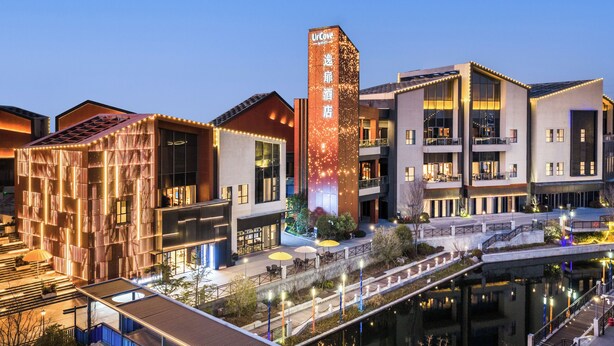 A modern hotel with a prominent tower, outdoor seating, and a canal view. - UrCove by Hyatt Taicang South Railway (Suzhou)