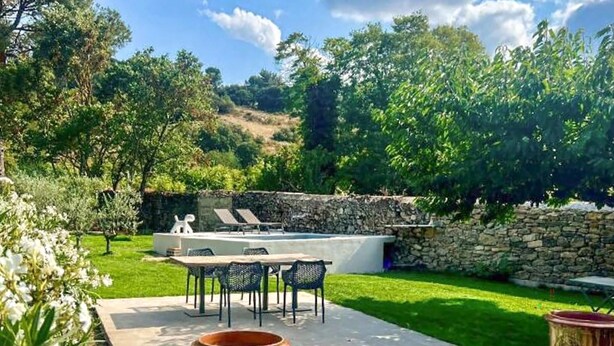 Une terrasse avec une table et des chaises, un mur en pierre et un espace piscine.