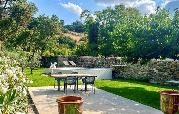 A patio with a table and chairs, a stone wall, and a pool area. - Maison piscine proche Alpilles (Alleins)