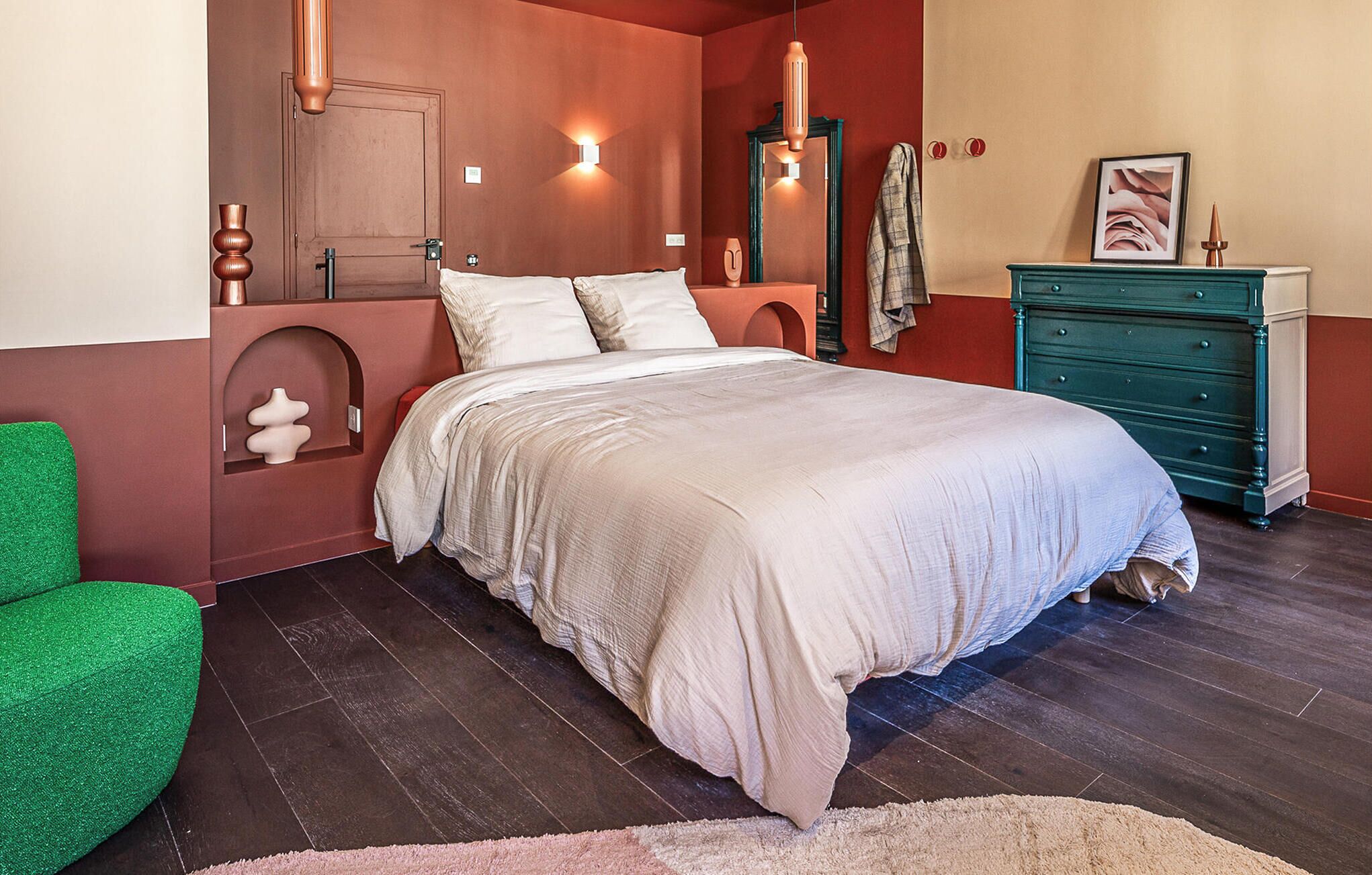 Une chambre à coucher avec un lit, une commode, un miroir et un fauteuil vert.