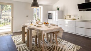 Une cuisine moderne avec des armoires blanches, un four encastré et un coin repas avec une table dressée pour quatre personnes.