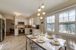 A modern kitchen with white cabinets, a central island with dining setup, and a large window with a view of trees. - Sunset Point 4 Bedroom Home by D&R canal (Princeton)