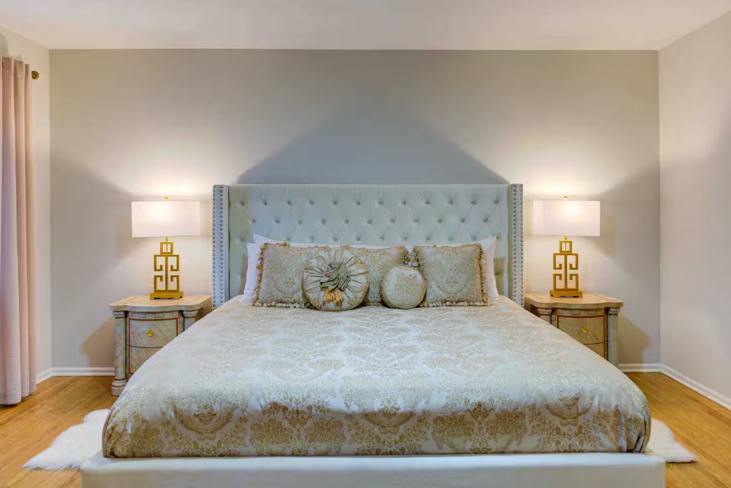 A large bed with a tufted headboard, two bedside tables with lamps, and a light-colored wall.
