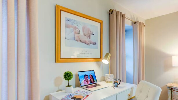 Ein ordentlich eingerichteter Raum mit einem gerahmten Bild, einem Laptop, einer kleinen Pflanze, einer Lampe und einem Stuhl.