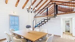 Ein Essbereich mit einem Holztisch, Stühlen, einer Kandelaber und einer Treppe mit Metallgeländer.