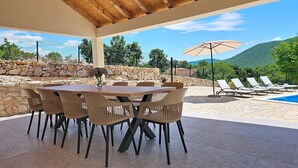 Eine Terrasse im Freien mit Tisch und Stühlen, einem Pool und Blick auf Berge.