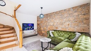 Ein Wohnzimmer mit Stehwand, einem grünen Sofa, einem Fernseher und einer Holztreppe.