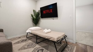 Ein kleines Zimmer mit einem Einzelbett, einem an der Wand montierten Fernseher und einem Blumentopf.