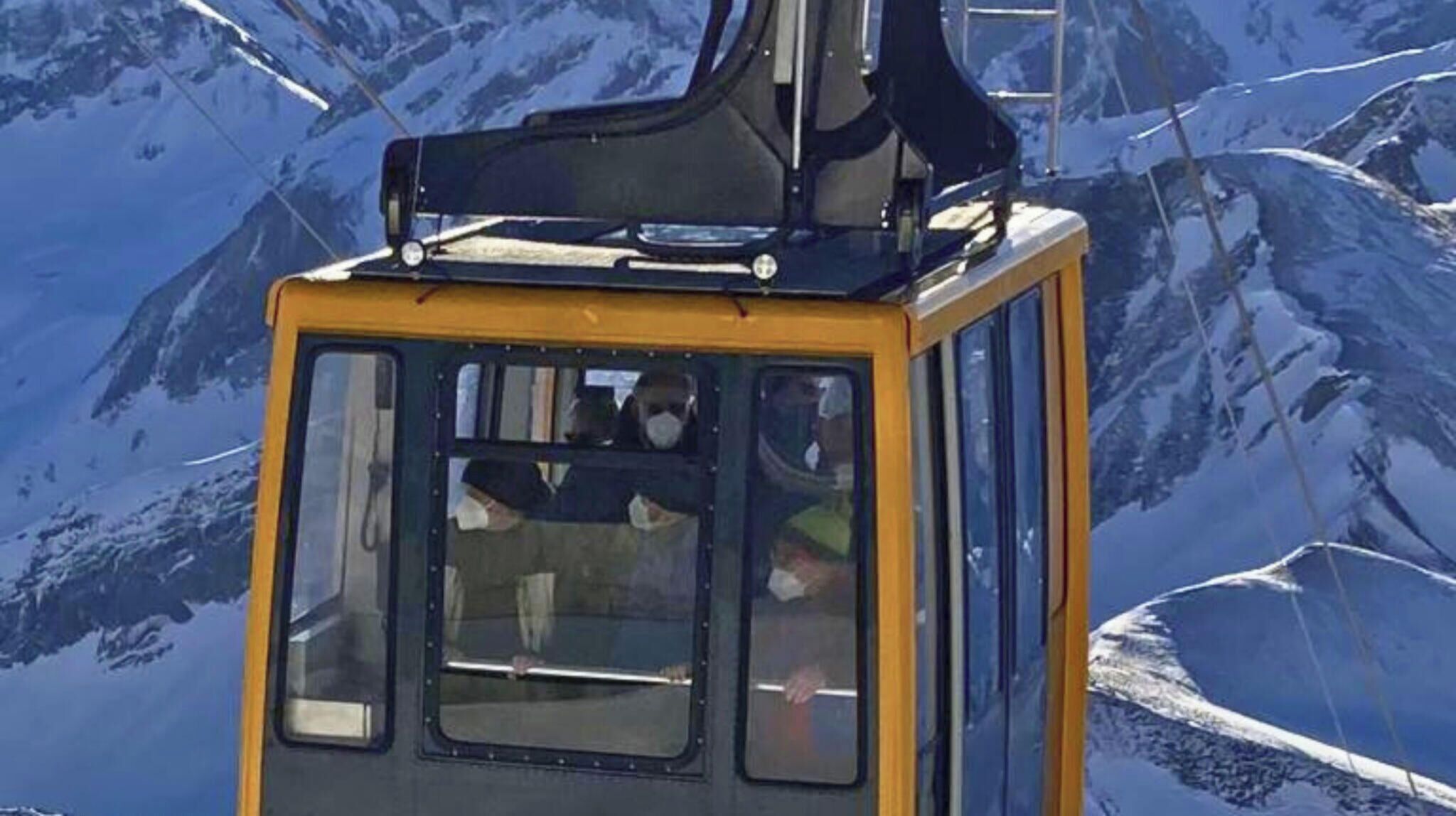 Una funivia con esterno giallo e nero, finestre e struttura metallica sulla parte superiore, sullo sfondo di una montagna innevata.