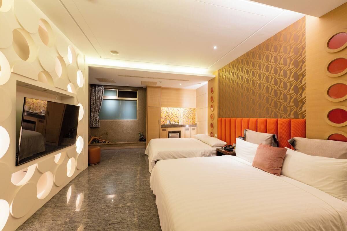 A hotel room with two beds, a TV, a bathroom, and a patterned wall.