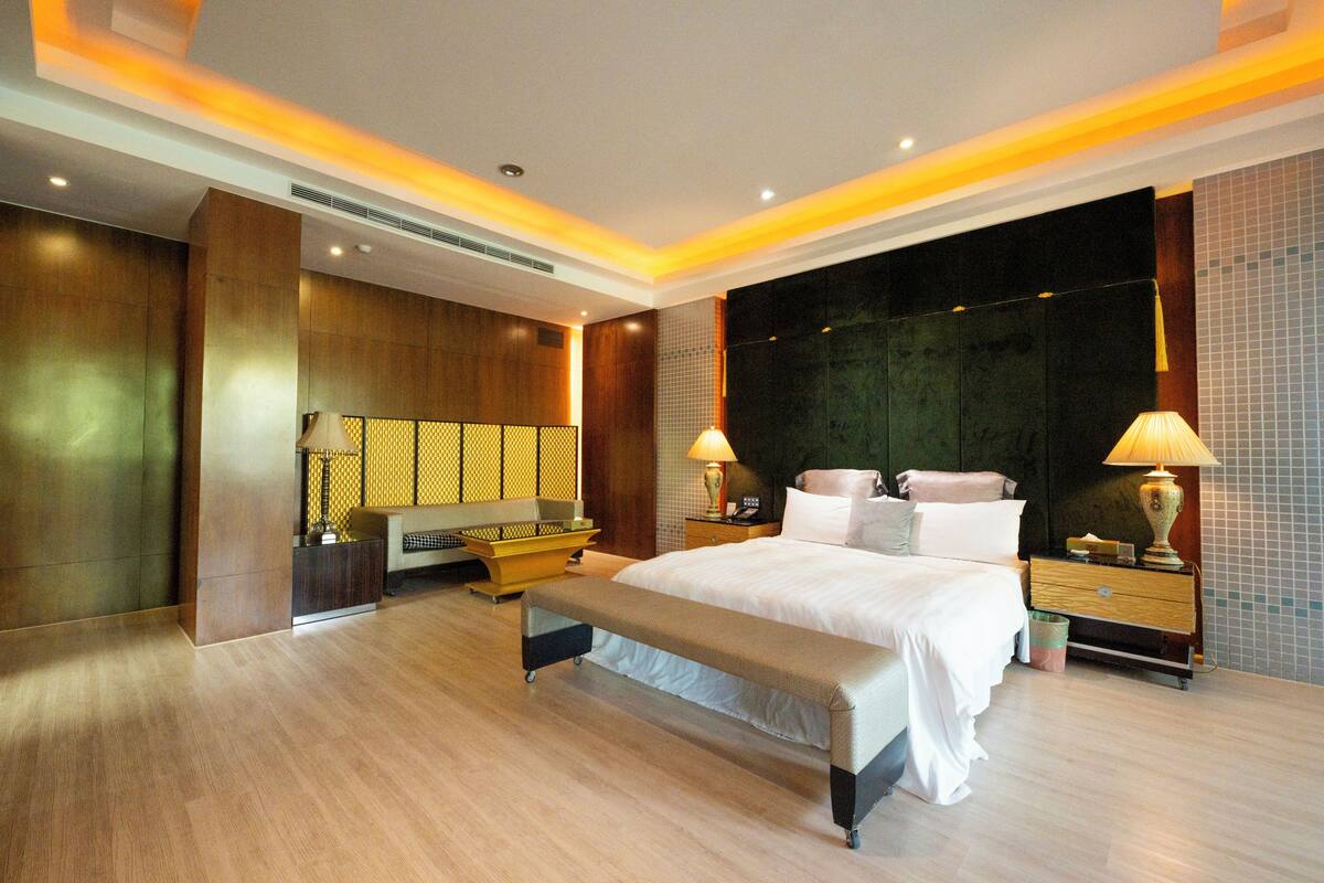 A modern hotel room with a large bed, bedside tables, a bench, and a large mirror.