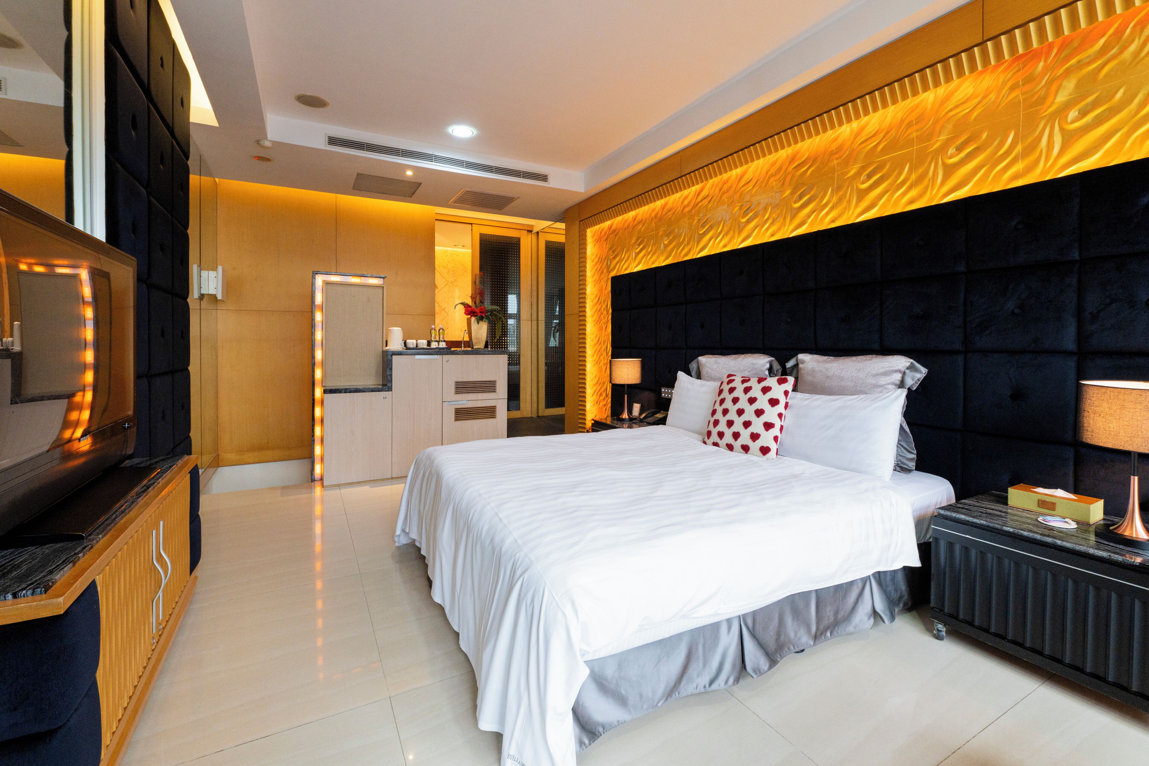 Habitación de hotel moderna con una cama grande, un televisor, una tocador y un baño al fondo.