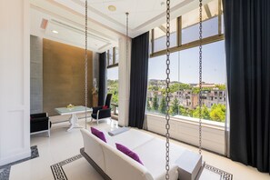 Una habitación de hotel moderna con una cama grande, una silla colgante, una mesa de comedor y vistas a la ciudad.
