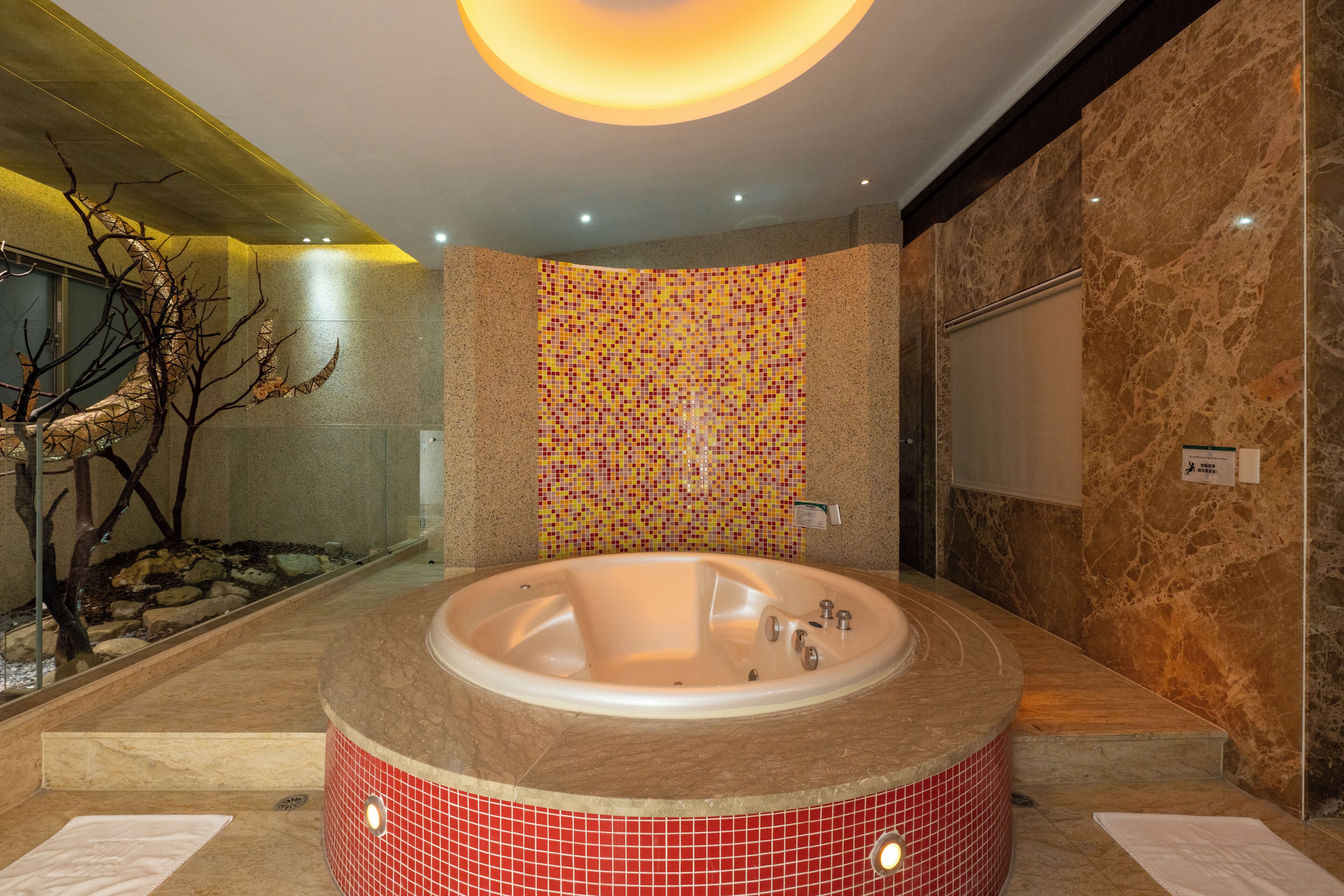Une salle de bain moderne avec une grande baignoire, un mur en mosaïque et une sculpture en forme d’arbre.
