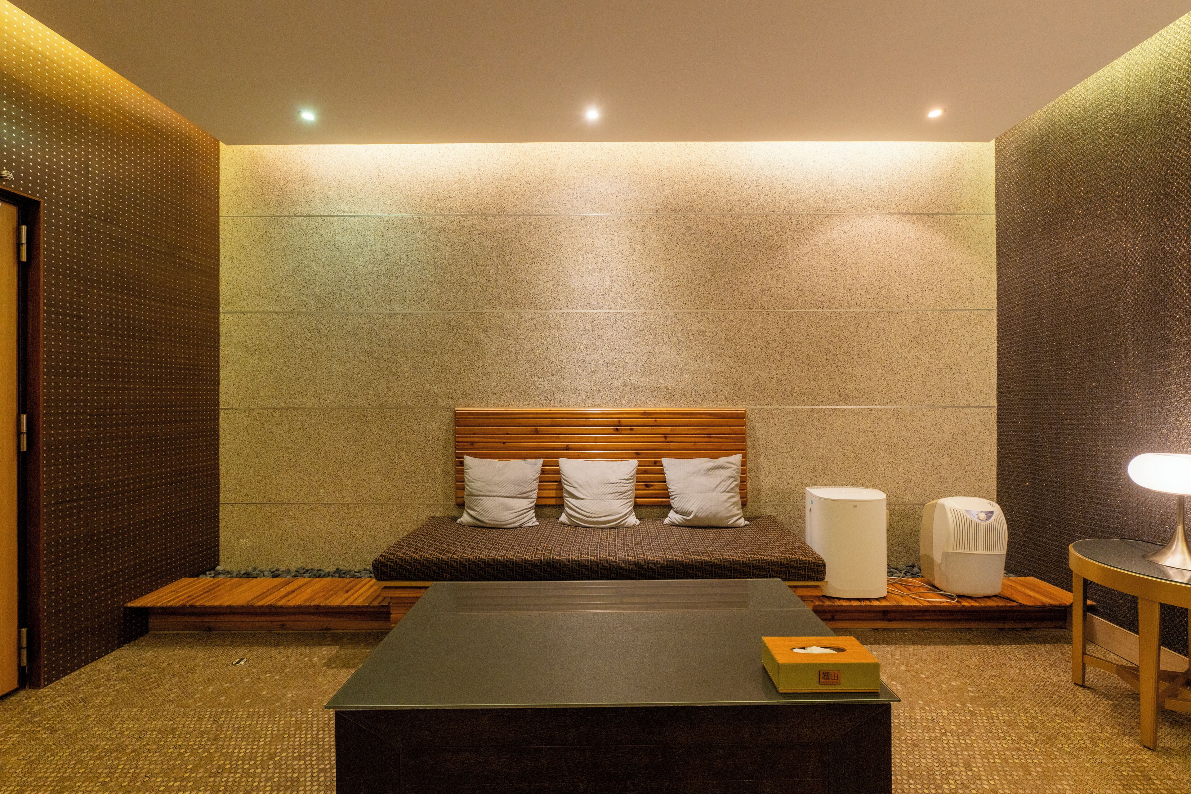 A modern hotel room with a bed, a bedside table, a lamp, and a wall-mounted air purifier.