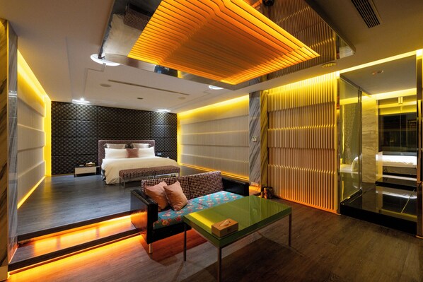 A modern hotel room with a bed, a sofa, a glass partition, and a wooden floor.