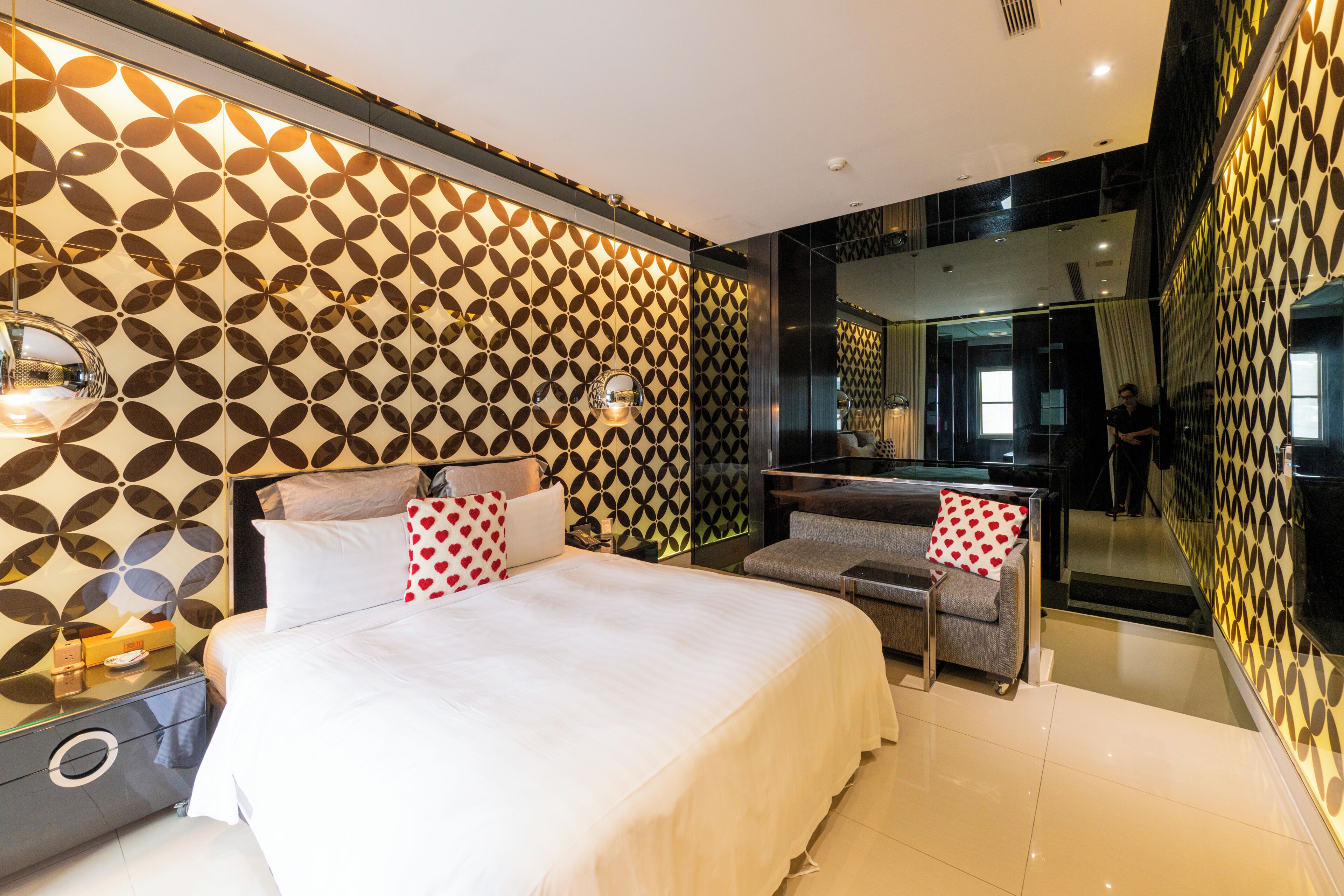 A modern hotel room with a large bed, a sofa, a mirror, and patterned walls.