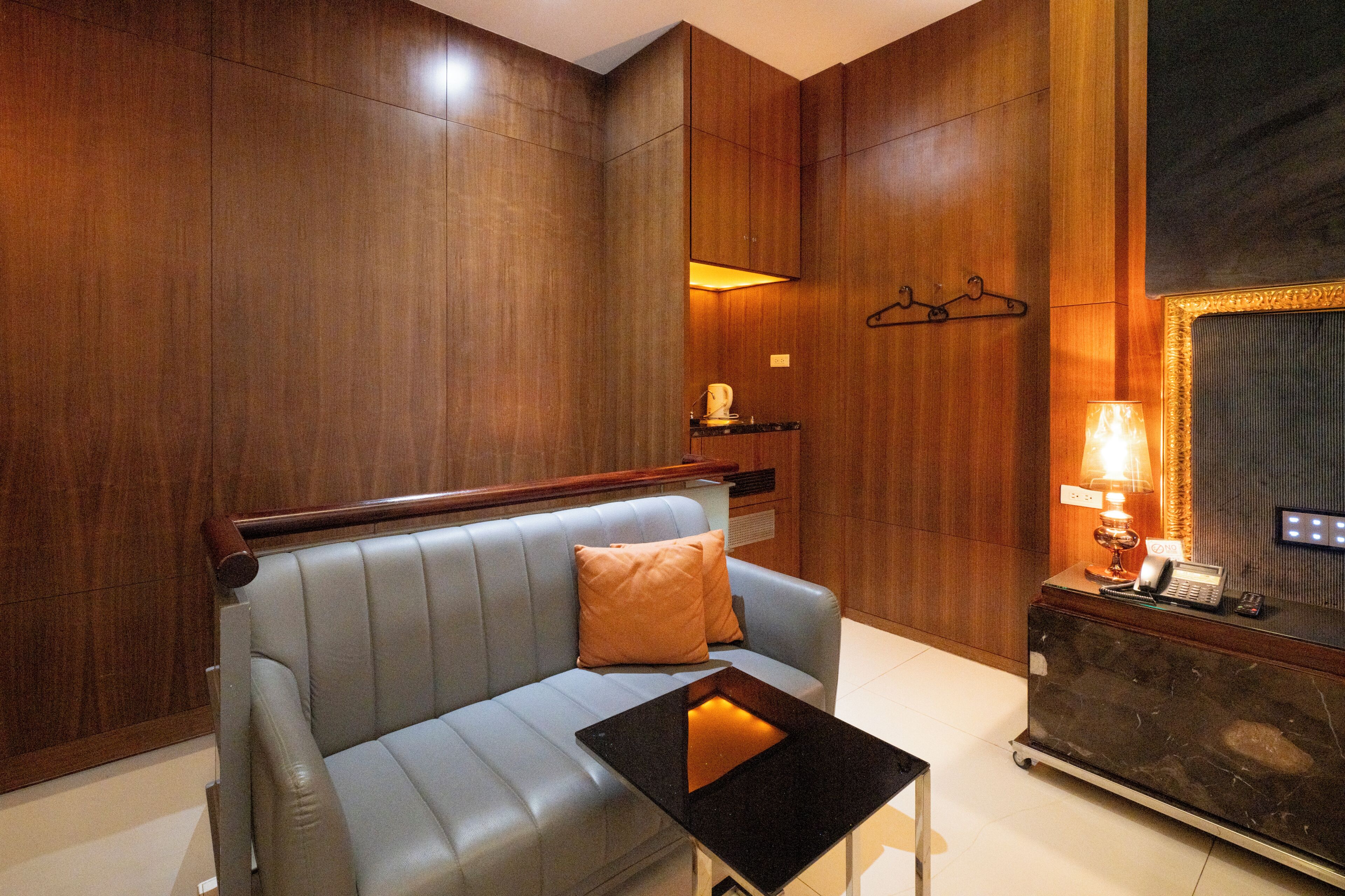A modern hotel room with a leather sofa, a small table, a lamp, and a reception desk.