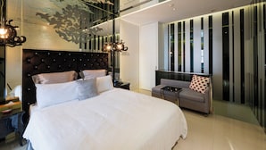 Una camera d'albergo moderna con un letto grande, un divano, un tavolino e un soffitto decorato.