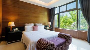 A modern hotel room with a large bed, bedside tables, a nightstand, a chair, and a large window offering a view of trees.