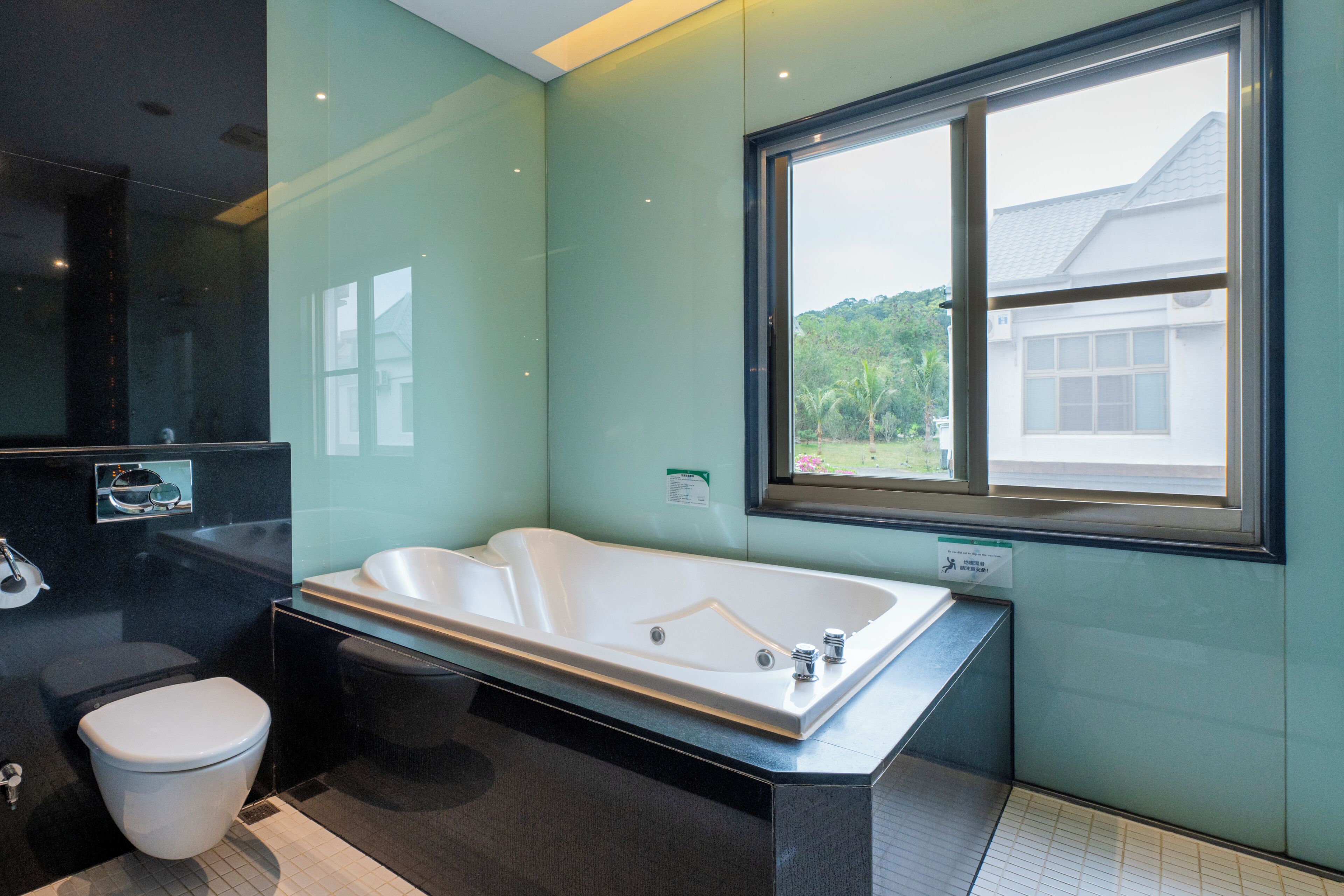Un baño moderno con una bañera grande, un inodoro y un ventanal con vistas a zonas verdes.