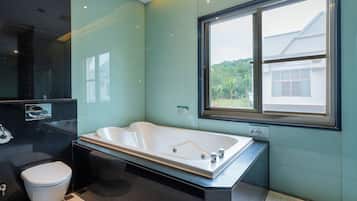Un baño moderno con una bañera grande, un inodoro y un ventanal con vistas a zonas verdes.
