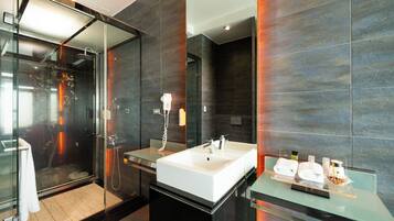 A modern bathroom with a glass shower enclosure, a large white sink, and a glass countertop with toiletries.