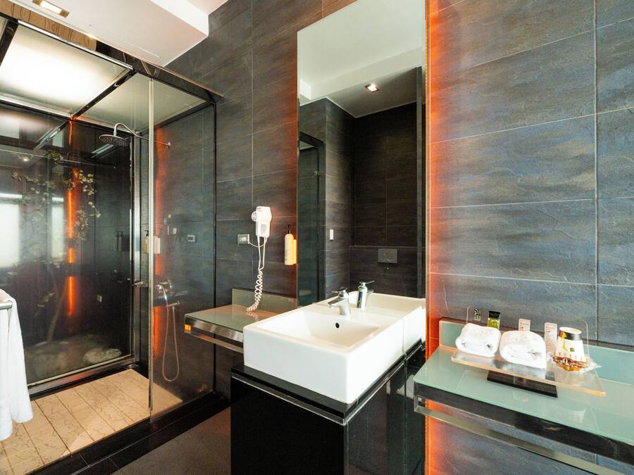 A modern bathroom with a glass shower enclosure, a large white sink, and a glass countertop with toiletries.