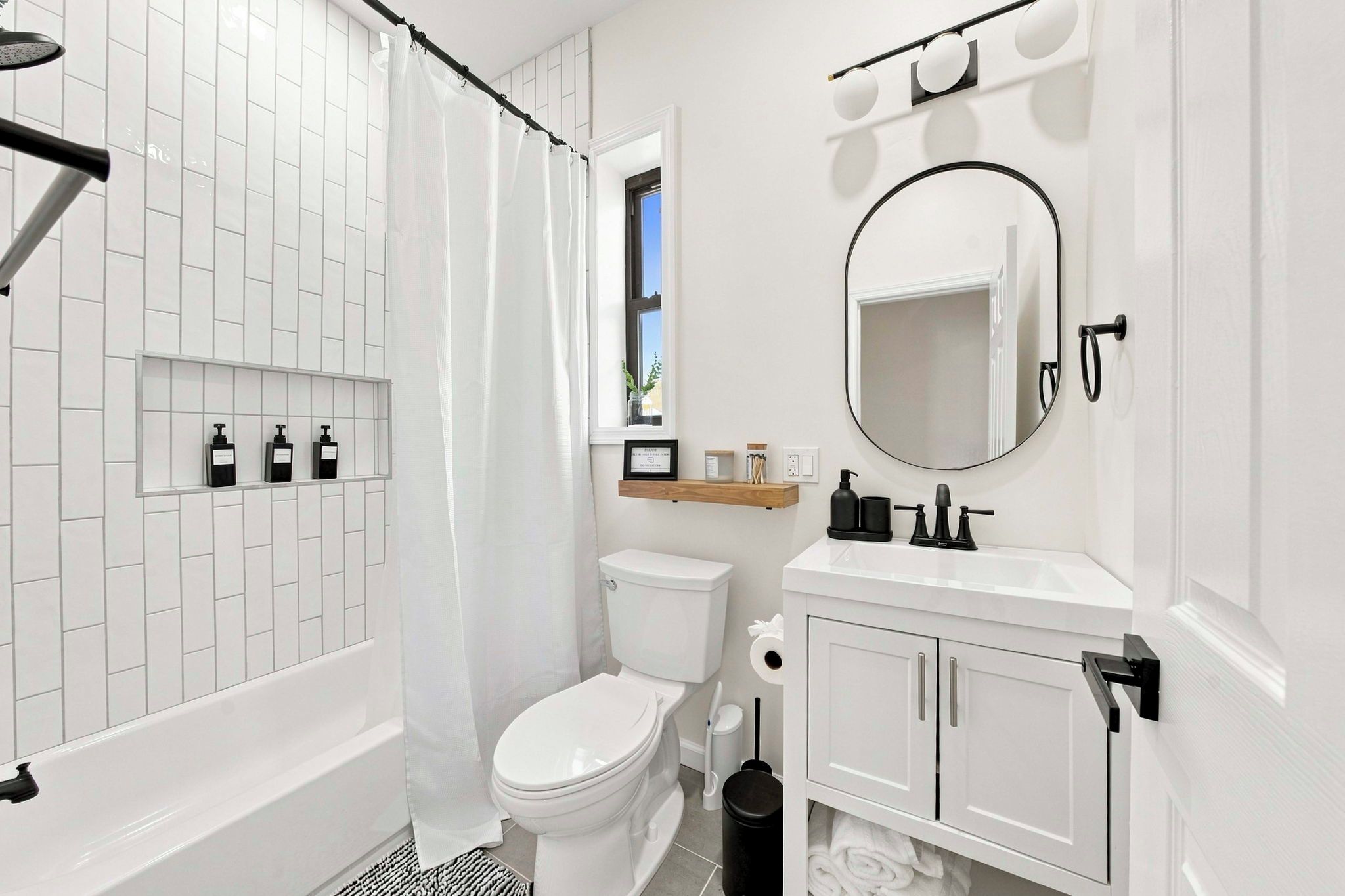 Een moderne badkamer met een witte betegelde douche, een toilet, een wastafel met spiegel en een plank met toiletartikelen.