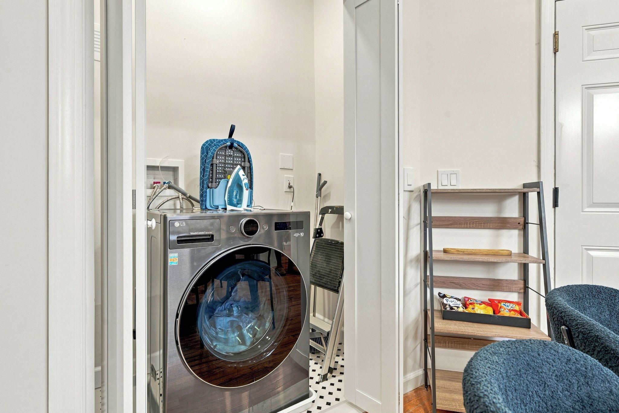 Een kleine wasruimte met een voorlader wasmachine, een droogrek en een klein plankje met snacks.