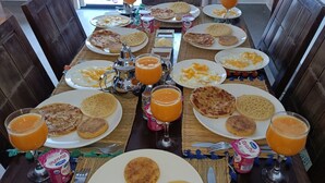 Una mesa de comedor servida con platos de comida, vasos de zumo de naranja y un envase de yogur.