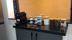 Una cocina con cafetera, tazas y recipientes sobre la encimera.