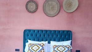 Una cama con cabecera capitonada, dos almohadas estampadas y una manta azul.