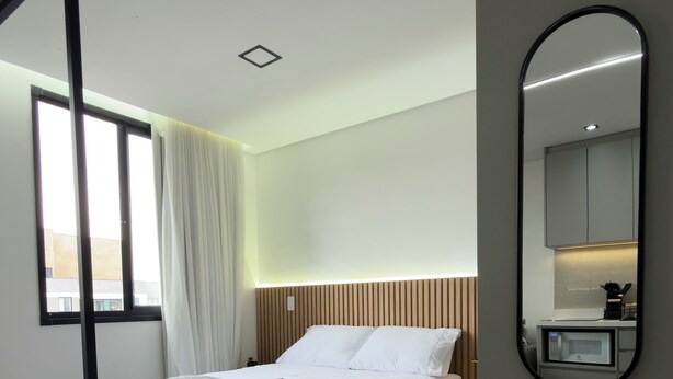 Een moderne hotelkamer met een bed, nachtkastje, spiegel en een raam met gordijnen.
