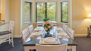 Uma sala de jantar com mesa de vidro, cadeiras brancas e um vaso de flores.