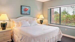 Quarto com cama, duas mesas de cabeceira com abajures, janela com persianas e um quadro na parede.