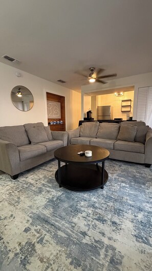 Ein Wohnzimmer mit einem Ecksofa, einem runden Couchtisch und einem Deckenventilator.