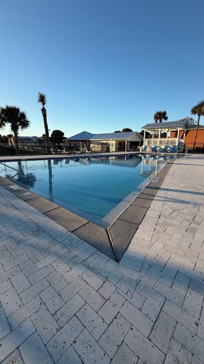 Une piscine avec une terrasse carrelée, des palmiers et, au fond, un bâtiment doté d’un toit en pente.