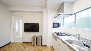 Ett modernt kök med en platt-TV, sopkorgar i rostfritt stål, en gasspis och ett stort fönster.