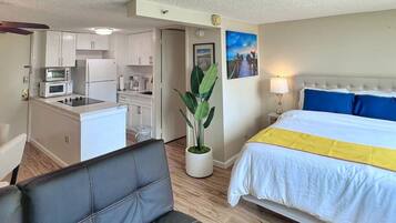 A hotel room with a bed, a small kitchenette, a dining area, and a living space.