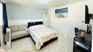 A bedroom with a bed, a sofa, a desk, and a painting of a beach.