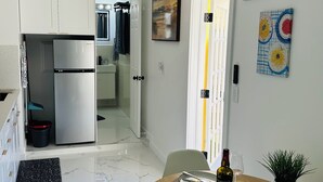 A modern kitchen with a refrigerator, a dining table with a wine bottle, and a potted plant.