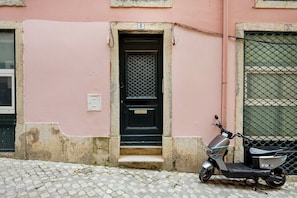 Uma scooter estacionada em frente a um prédio com porta numerada e portão de metal.