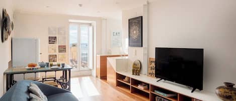 En moderne stue med sofa, fjernsyn, træhylder og et spiseområde med bord og stole.
