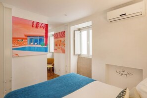 Ein Schlafzimmer mit einem Bett, einer blauen Bettdecke, einem Fenster und zwei Bildern an der Wand.